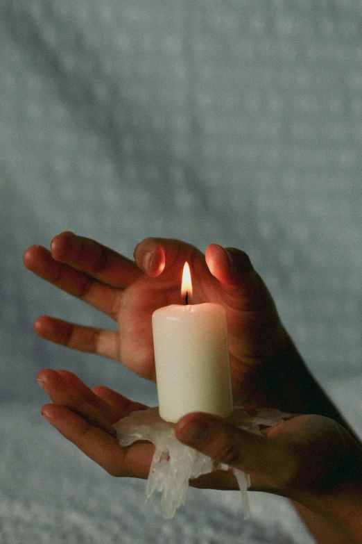 someone's hands holding a burning candle with both hands