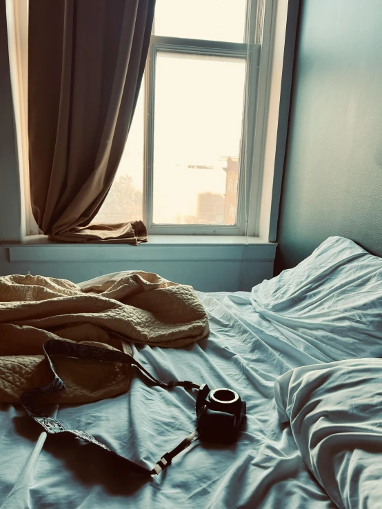 camera and purse sitting on the bed next to the window