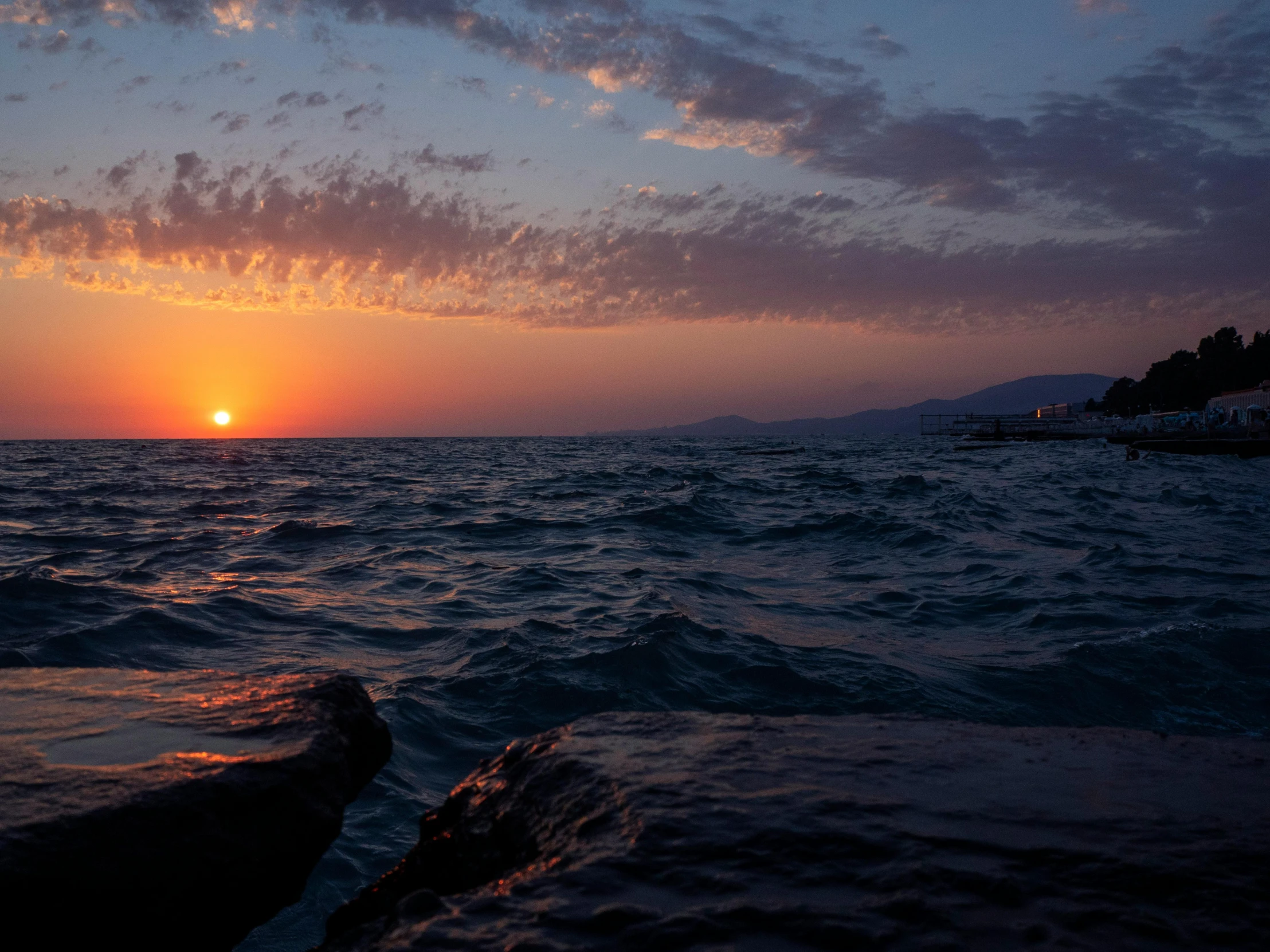 the sun sets over the water and a small boat