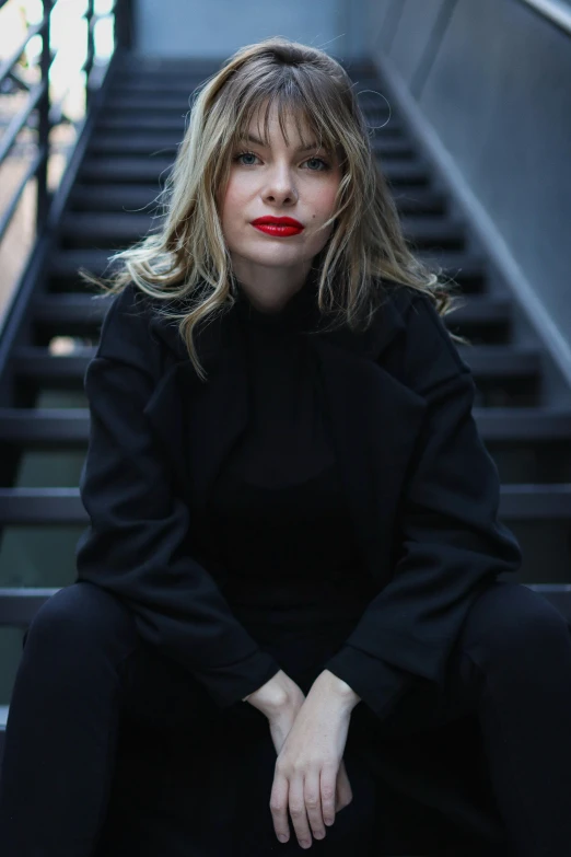 a woman sitting on some stairs with her hand in her pocket