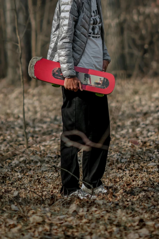 a boy holding his skateboard in the woods