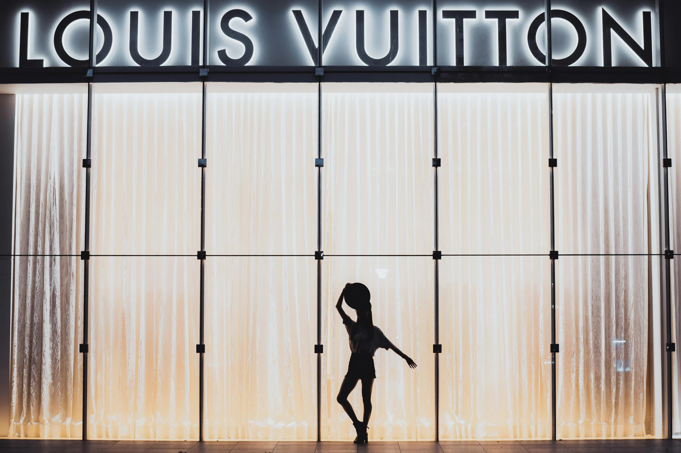 the silhouette of a woman walking past an illuminated sign