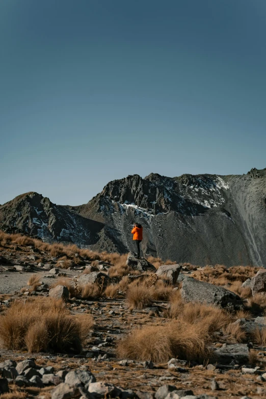 a person in an orange jacket standing at the base of a mountain