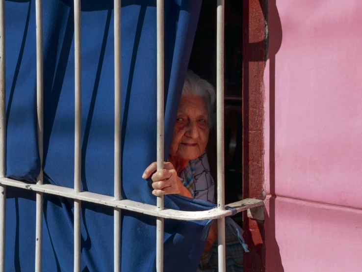 an elderly woman is peaking through the bars of her fenced in area