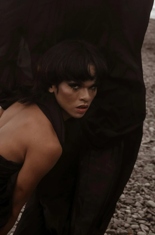 a woman with dark makeup stands close by some rocks