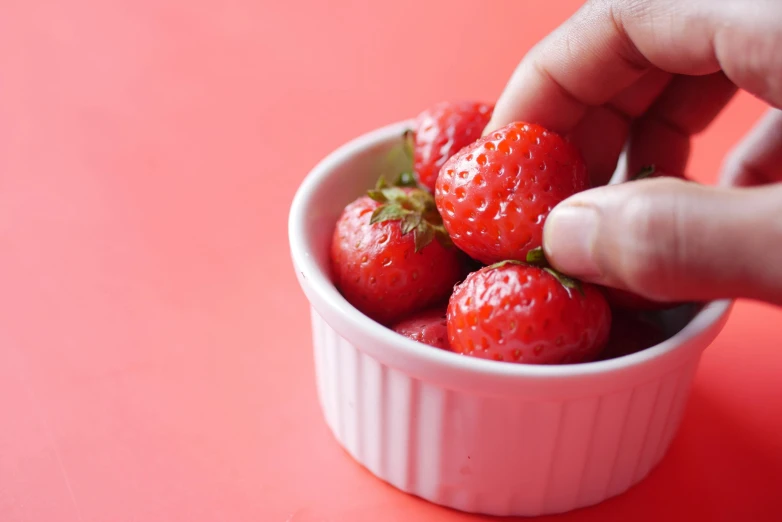 a person picking up strawberries in a white bowl