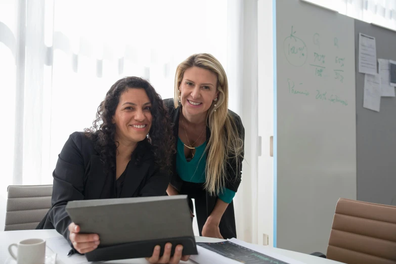 two women smile together over an electronic tablet