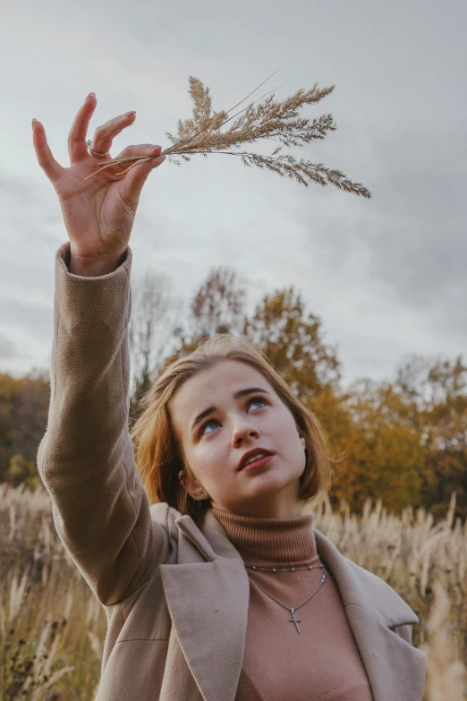 a girl holding up an oat stem on a cloudy day