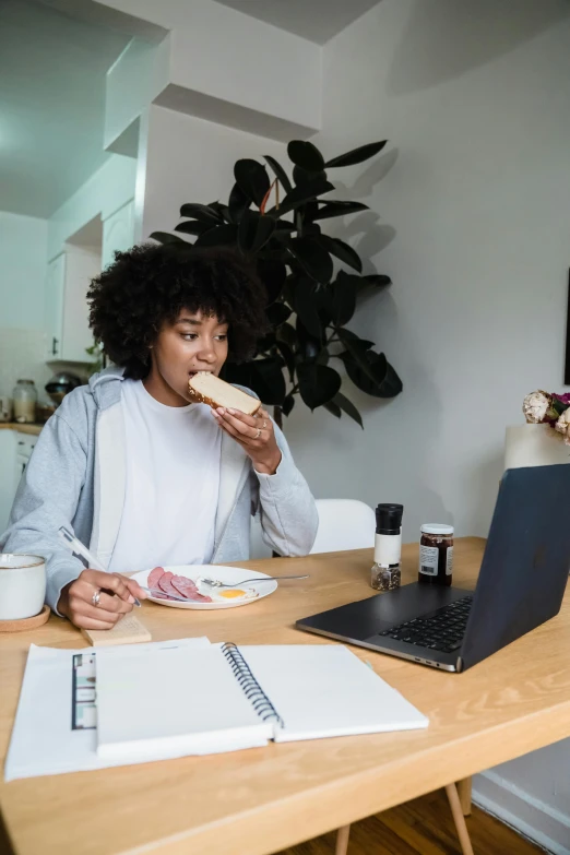 a young woman eats a sandwich at her desk