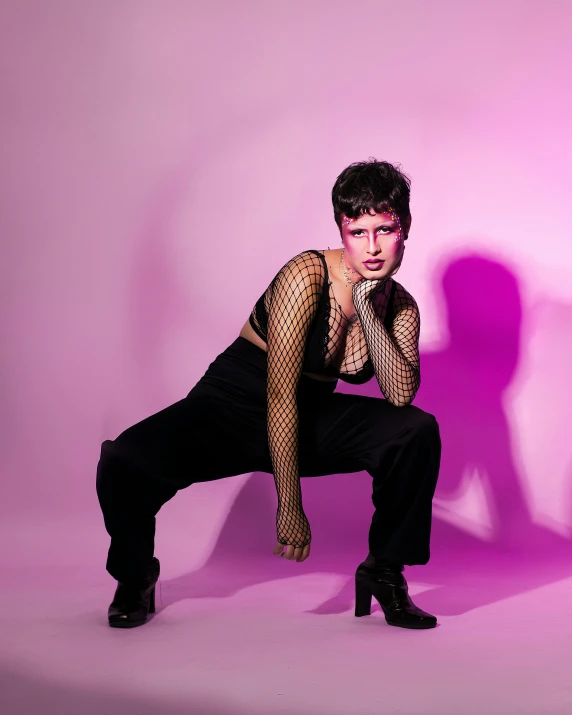 a young man in black is crouched down against a pink background