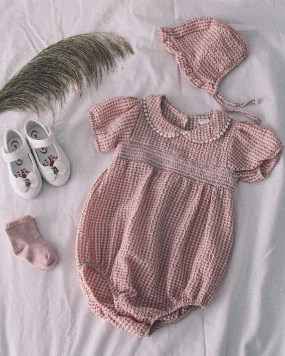 an infant girl's outfit, shoes and a feather laying on the bed