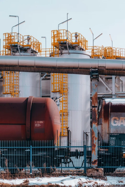 some metal tanks and train cars in front of a fence