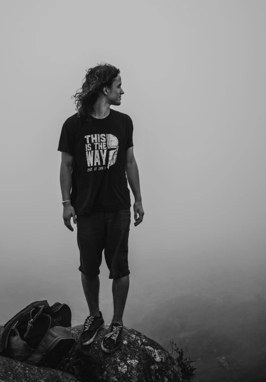 a young man standing on top of a mountain on a foggy day