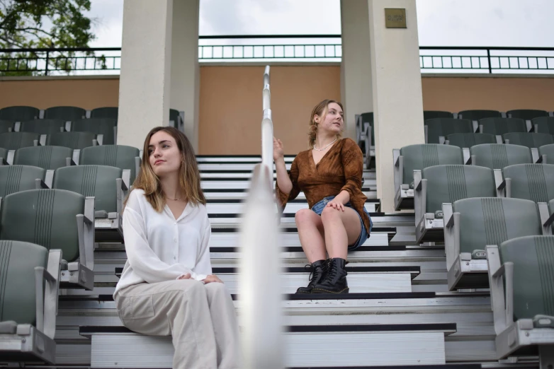 two women in their twenties sitting down on the bleachers