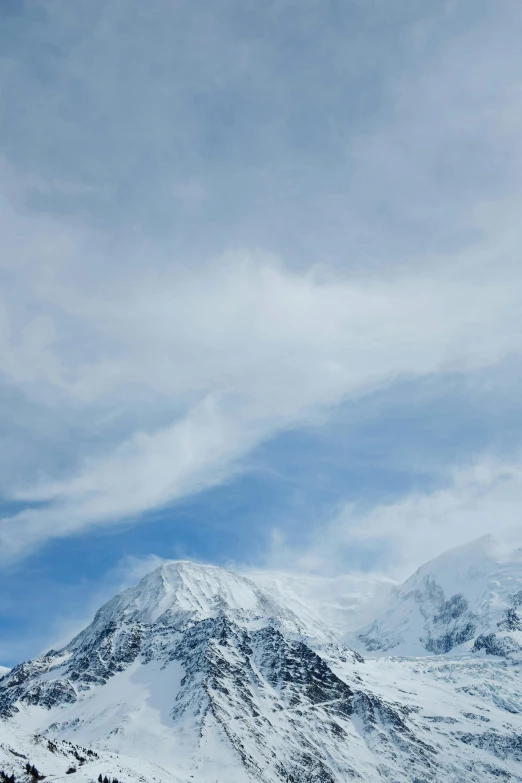 the mountain has many snow on it and there is a very large cloud in the sky above it