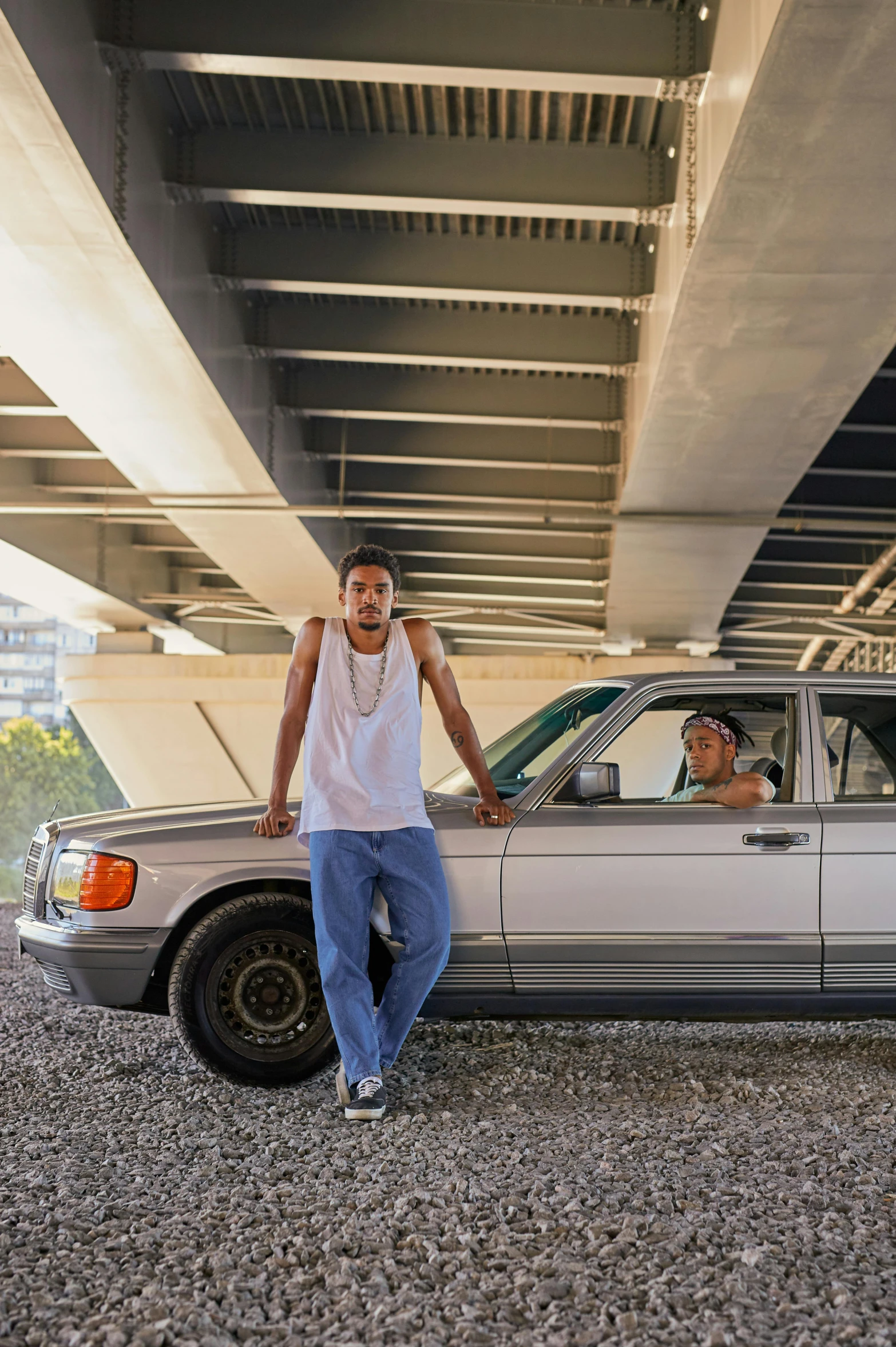 two men are posing by their car under a bridge