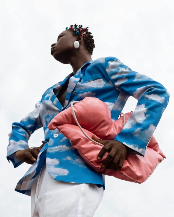 woman in blue and white coat holding pink bag looking up at sky