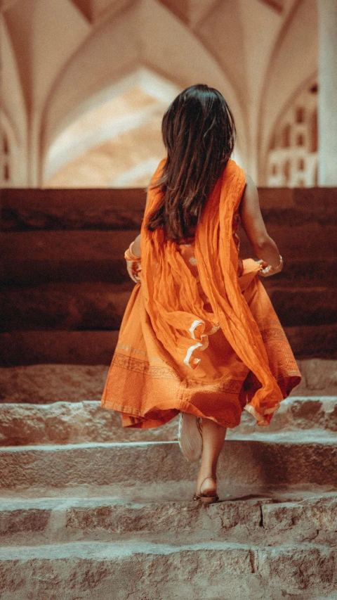 a  wearing an orange dress walking up some stairs