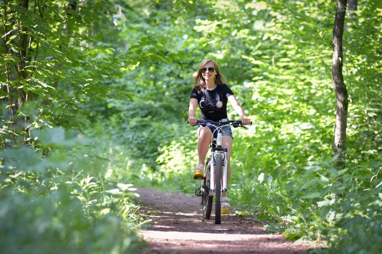 woman in sunglasses rides a bike down a path through tall grass and trees