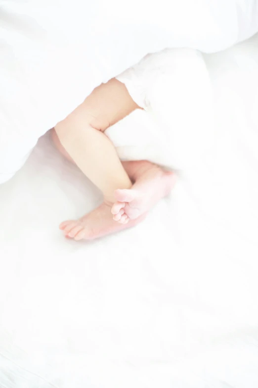 an infant's feet in the white blanket of a bed
