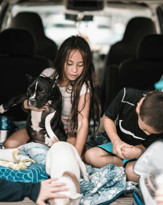 three children sitting in the back of a van holding and petting two dogs