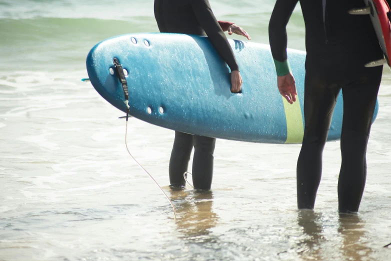 two men in wetsuits stand on the beach and hold their surf boards