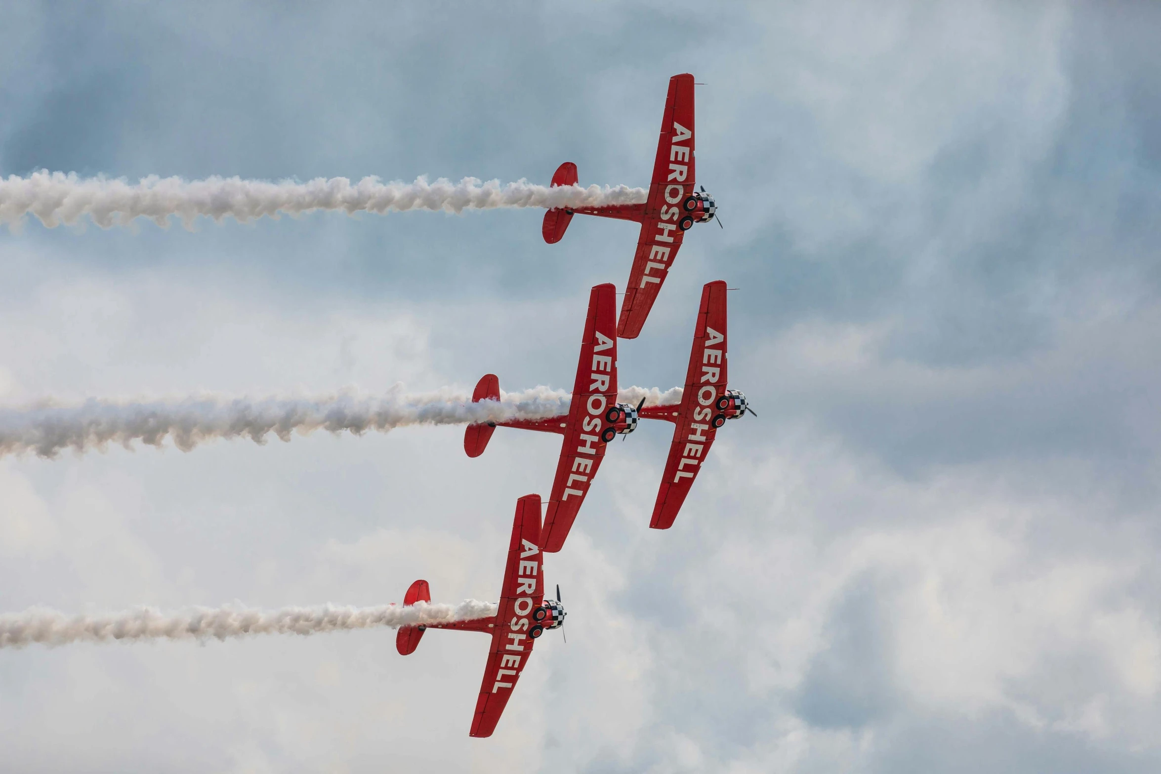 four red airplanes flying in formation with trailing smoke