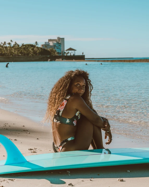 a woman kneeling next to a surfboard on the beach