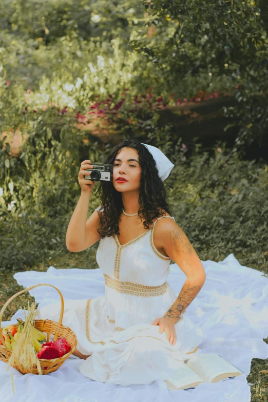 a woman sitting in the woods with an old camera and a picnic basket