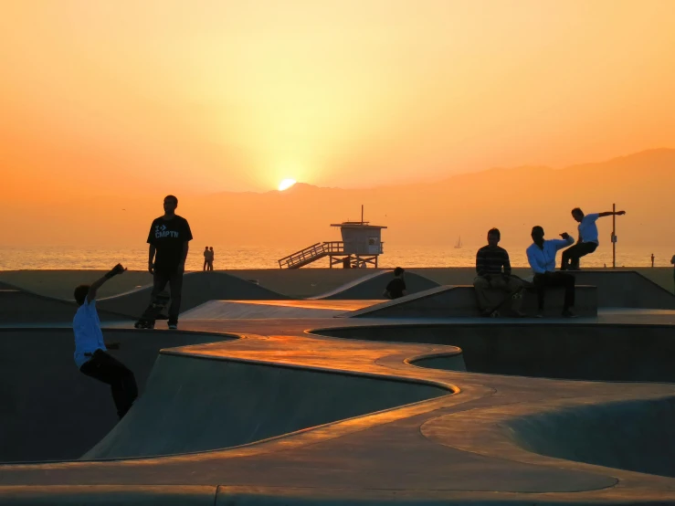 people in skateboards at a skateboard park with the sun setting in the background