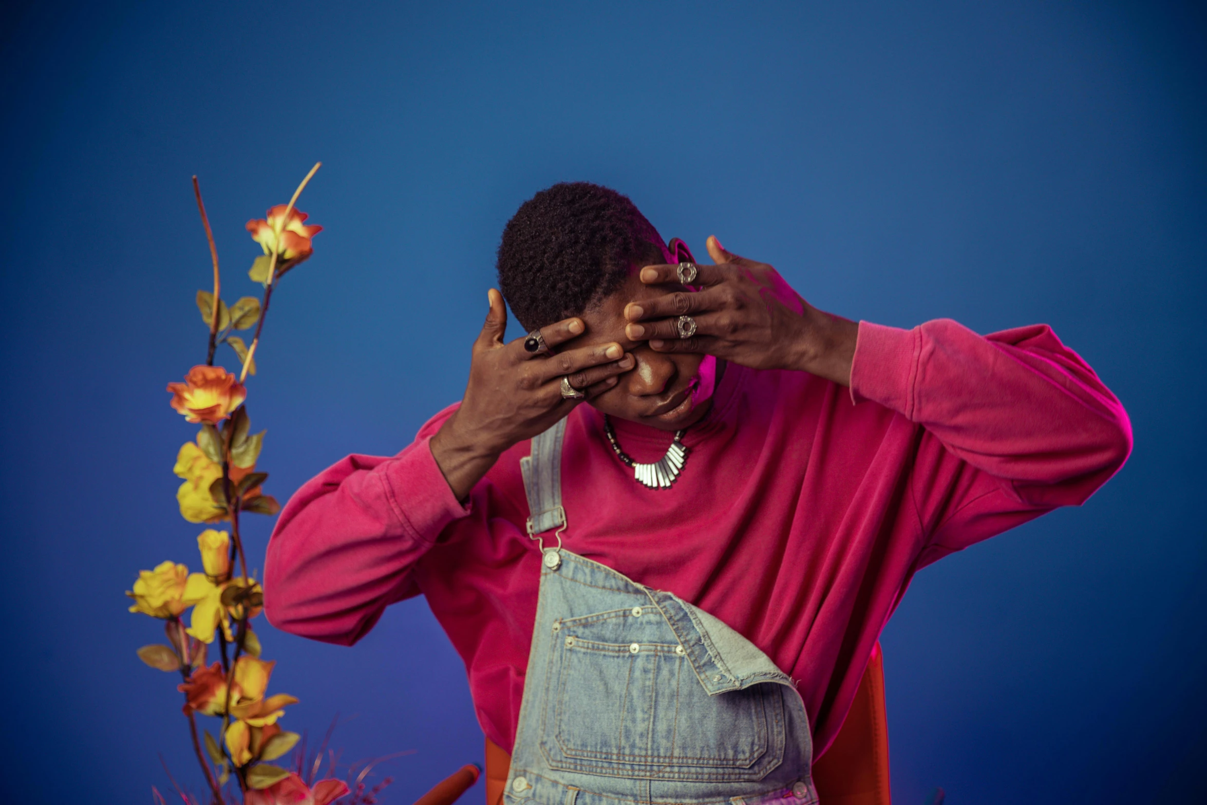 a man wearing overalls and a pink shirt is covering his eyes