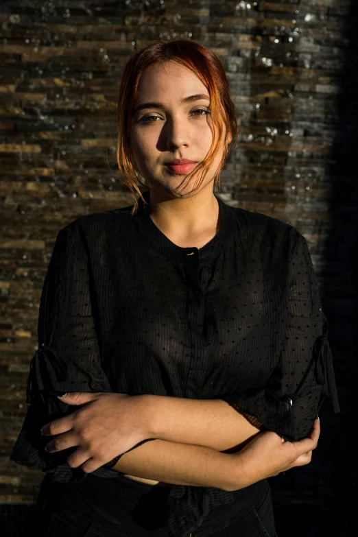 a woman posing with her arms crossed while a brick wall behind her