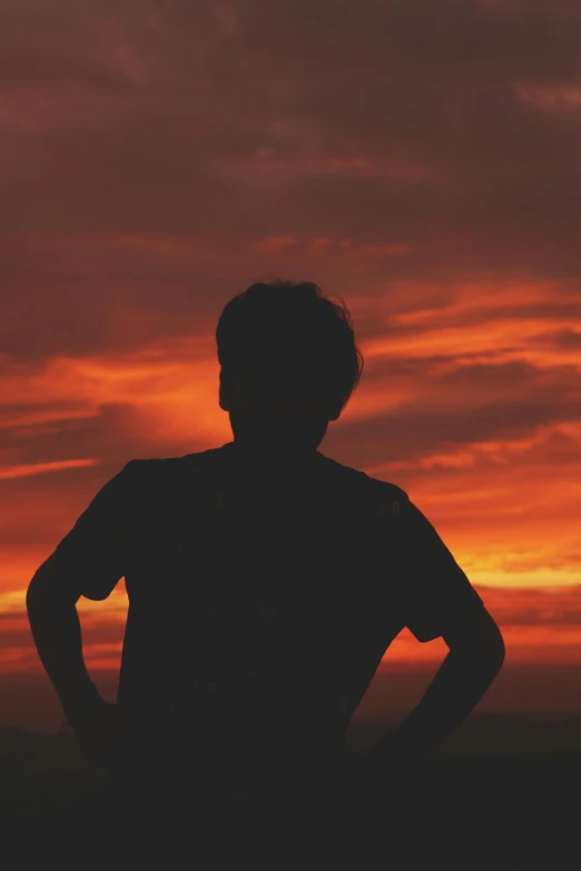 a man standing under a red sky watching the sun set