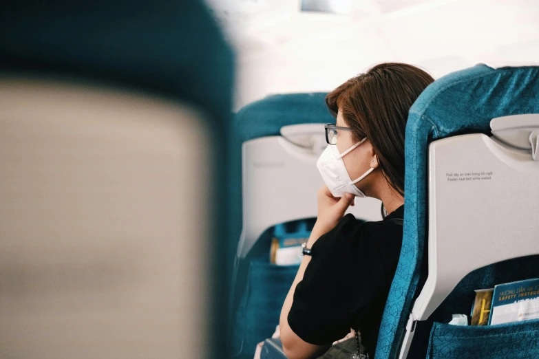 a woman in glasses sits on an airplane with a mask covering her mouth
