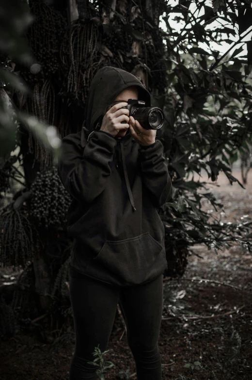 a girl taking pictures while standing in the woods
