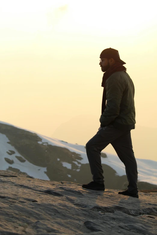 a man in cold weather gear and hat walking along a cliff