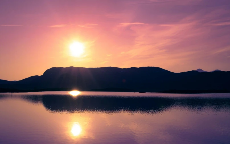 a beautiful purple sunset behind a mountain range with a lake