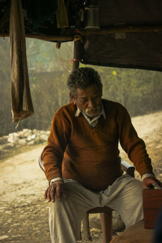 an older man is sitting by a tree and looking down