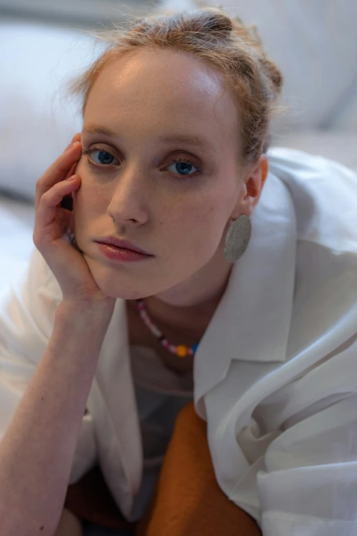 a young lady with a blonde hair wearing a white jacket sits on a bed