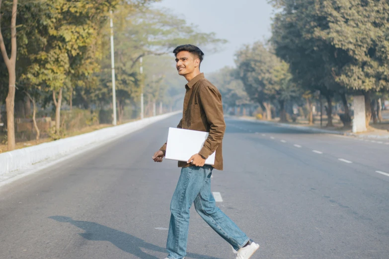 a young man crossing the street holding his laptop in hand
