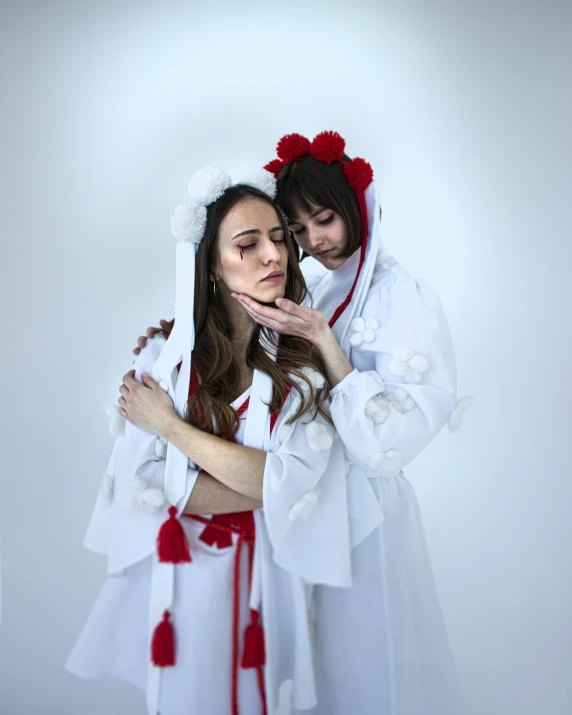 two woman dressed in white wearing head dresses and red head scarves