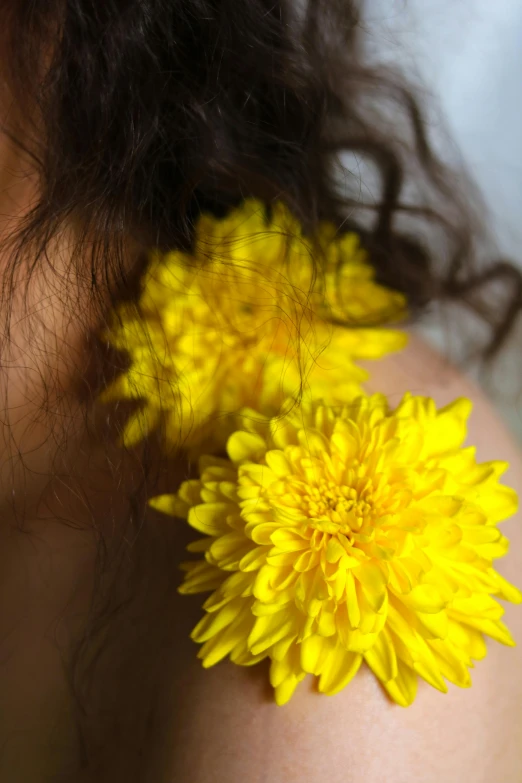 a person is holding two yellow flowers up to their neck