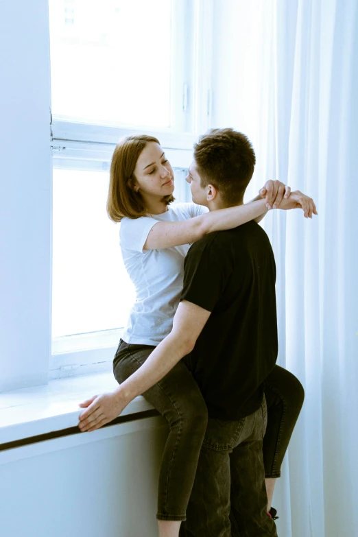 a young man hugs the woman in front of a window