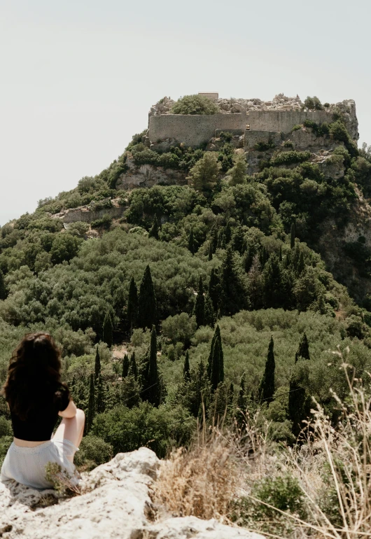 a person sits on top of a mountain overlooking a castle