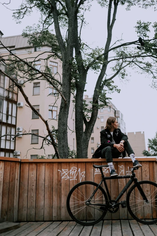 a boy sitting on a bike leaning against a wooden wall