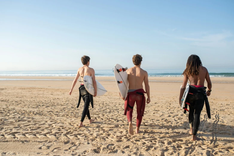 three people on the beach carrying their surfboards