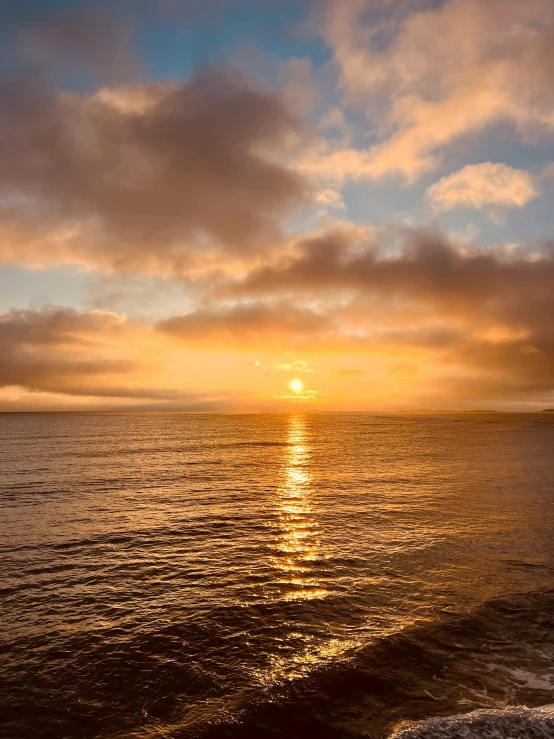 a lone surfboard is on the shore as the sun sets