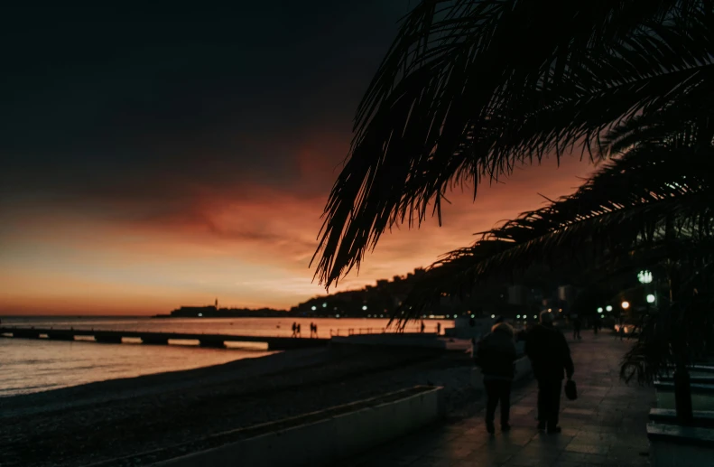 two people walk on the sidewalk at sunset