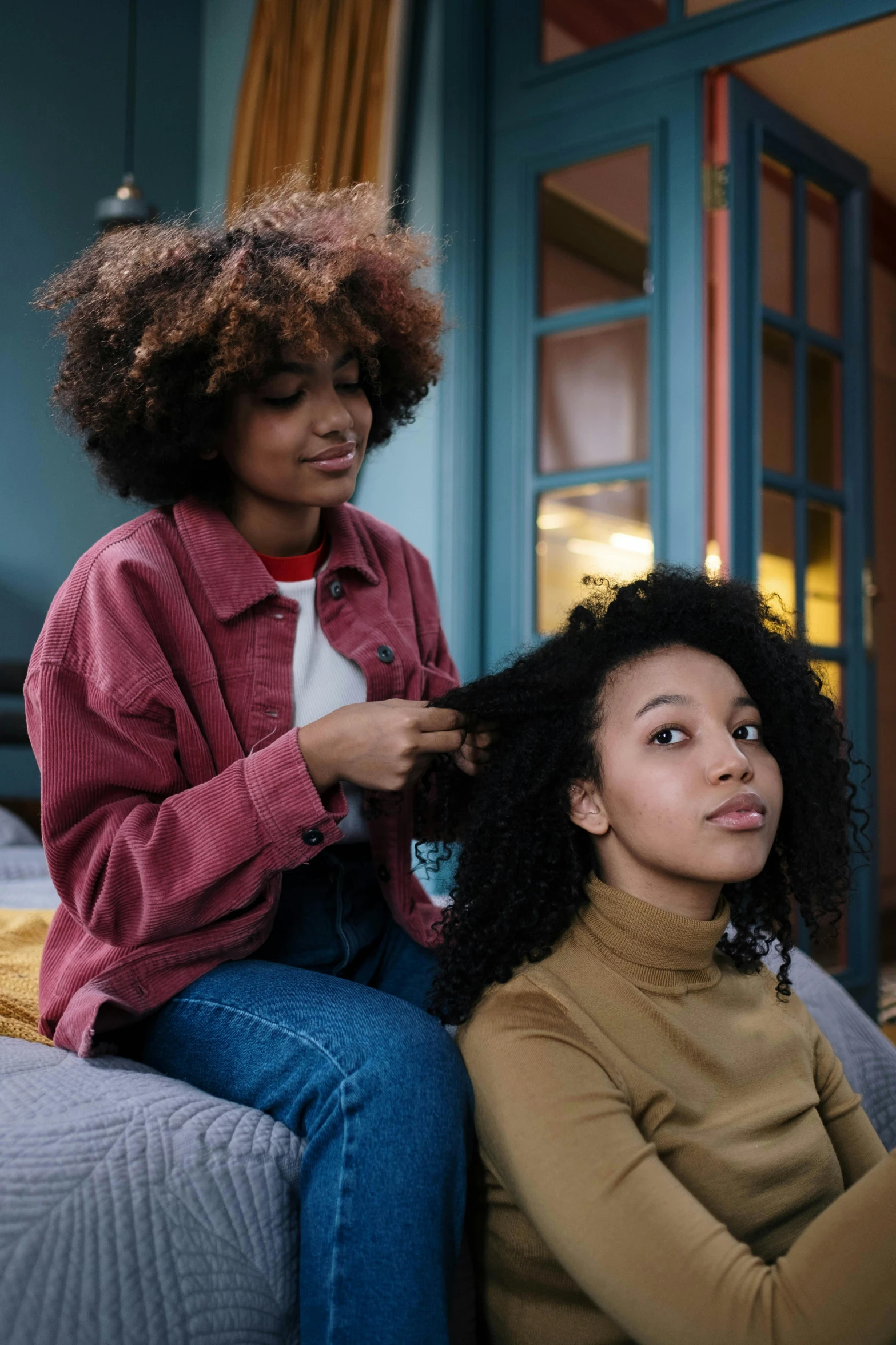 two women sitting on a bed one of which is blow drying her hair