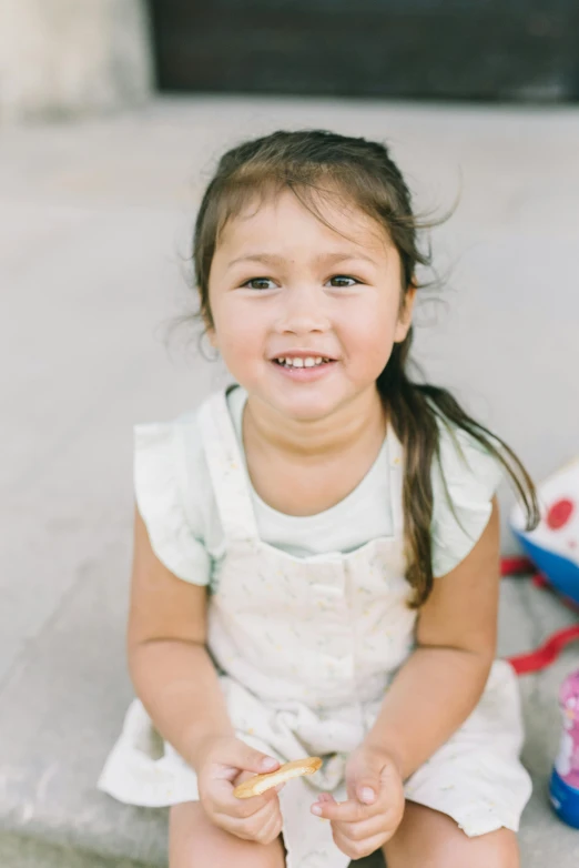 a little girl smiles sitting down with food in her hands